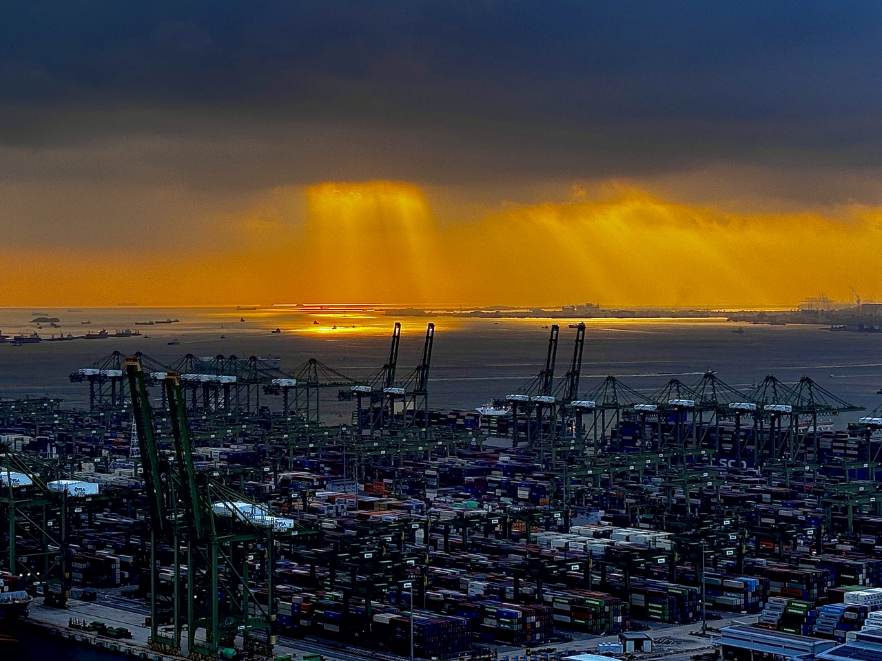 Container cranes and stacked shipping containers at Pasir Panjang Container Terminal in Singapore at sunset