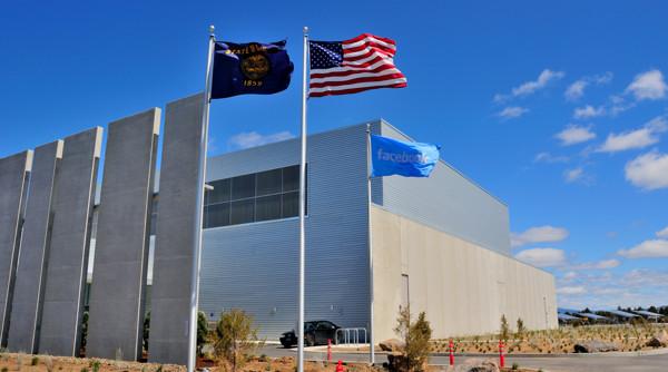 Exterior of a large data center building with US and state flags flying in front under a blue sky