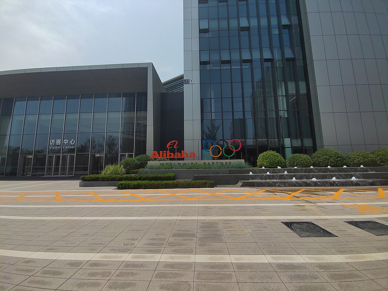 The entrance and visitor center at an Alibaba campus, with the Alibaba logo and Olympic rings on a low wall