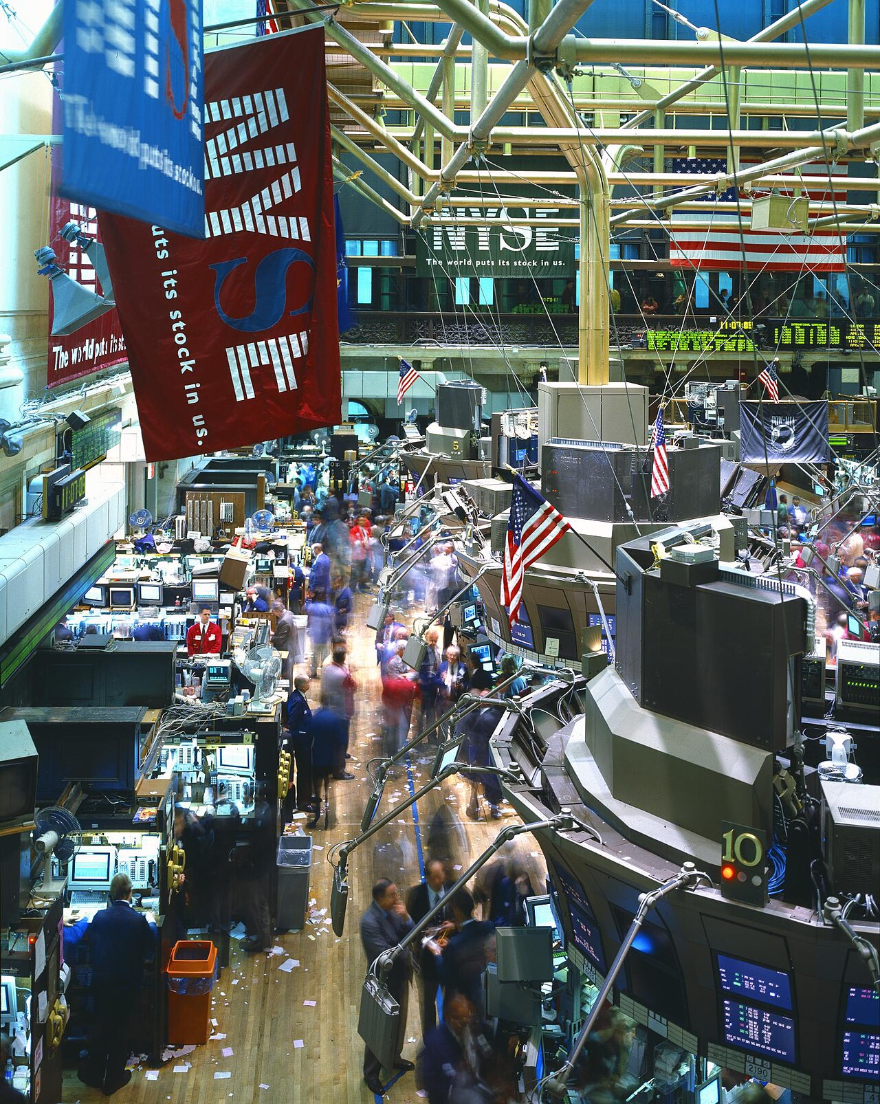 Interior view of the New York Stock Exchange trading floor, showing NYSE signage, an American flag, and trading posts