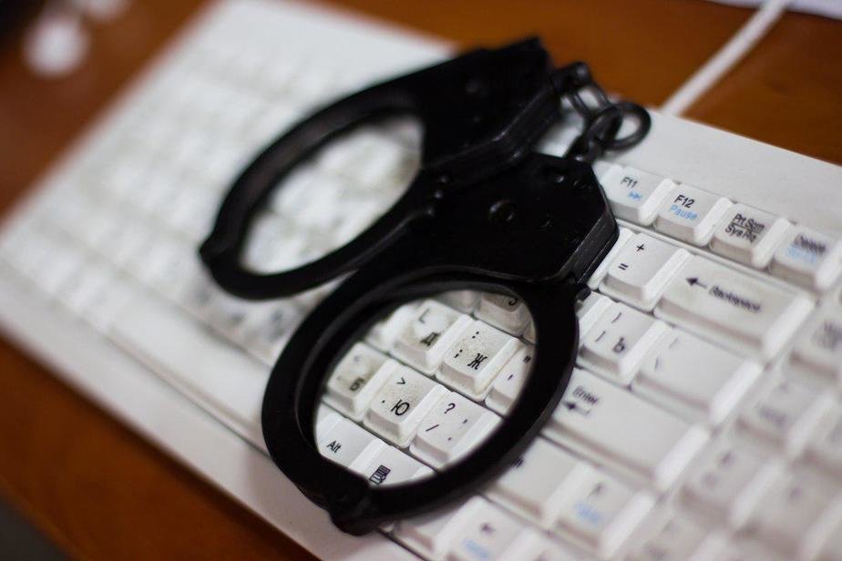 A pair of handcuffs resting on a computer keyboard, a common visual shorthand for cybercrime and unauthorized computer access