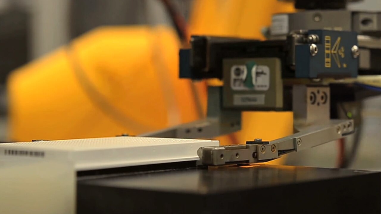 A robotic arm gripper positioned over a laboratory assay plate as part of an automated high-throughput screening workflow