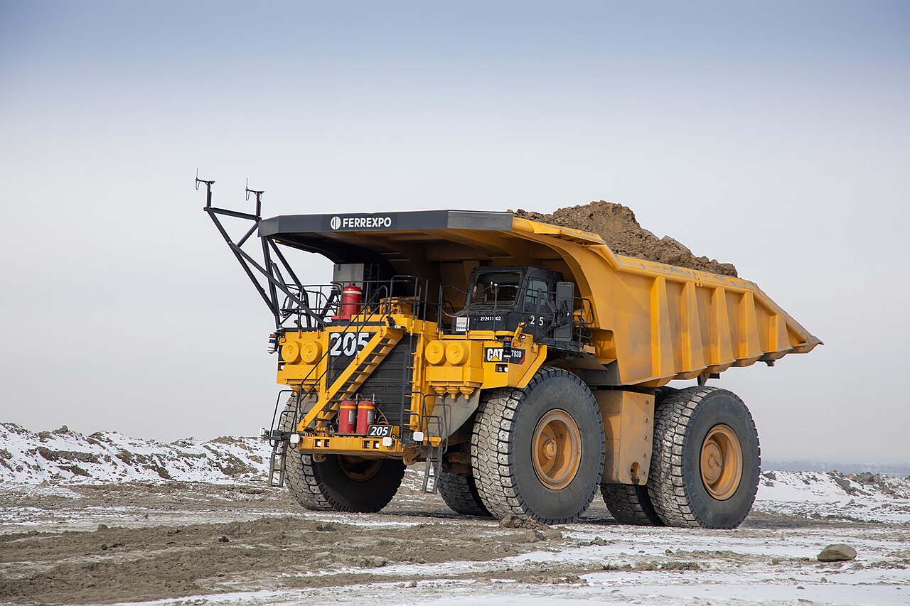 An autonomous mining haul truck with a visible sensor mast, loaded with ore, at an open-pit mine