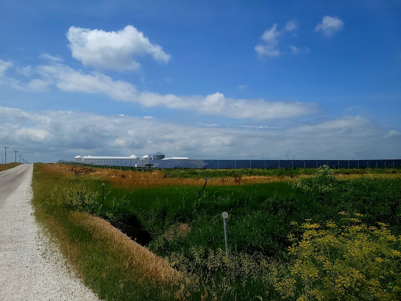 A large data-center campus on the plains with wind turbines visible behind it