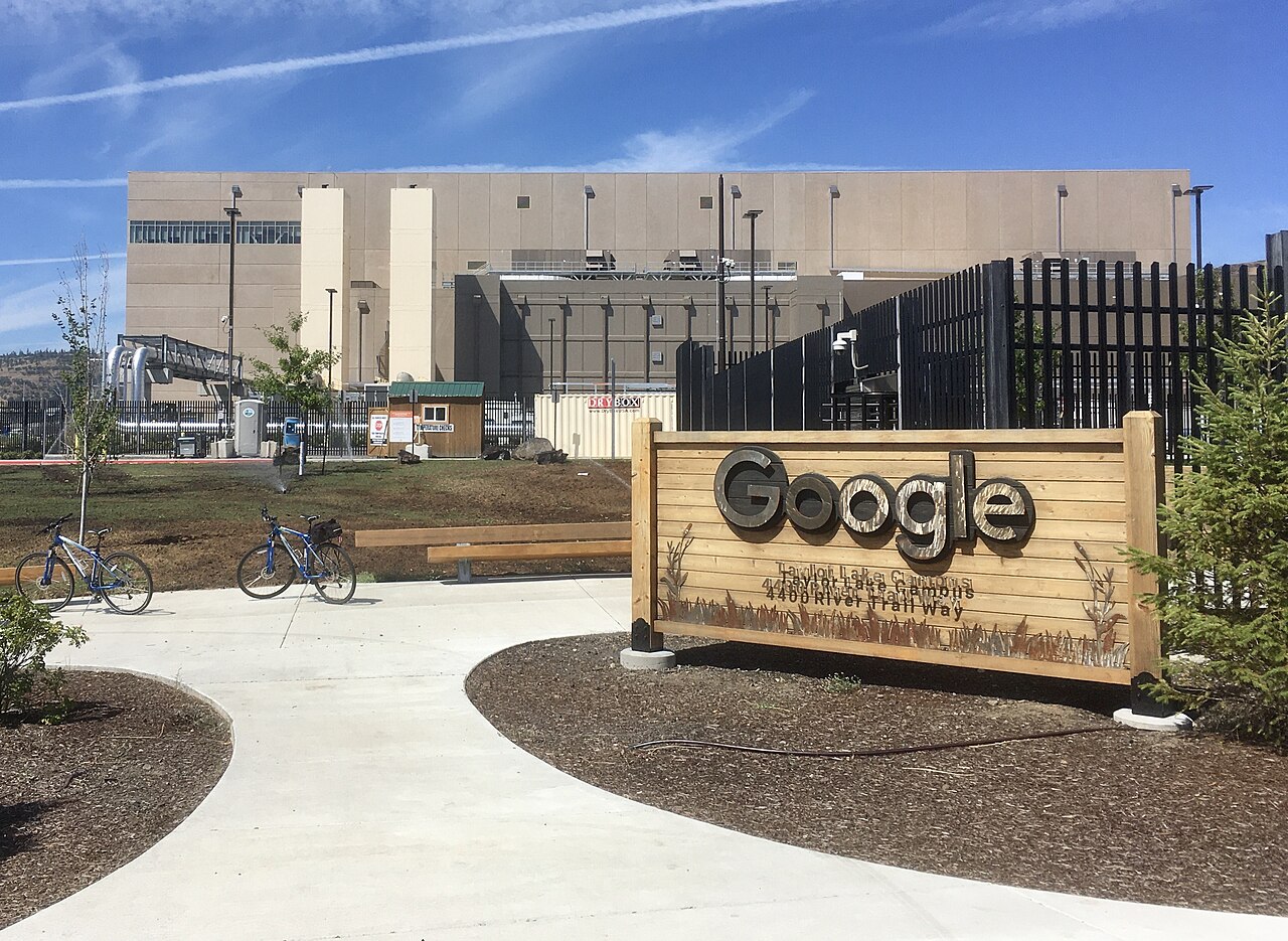 A Google data center building with signage, behind a fence on a clear day