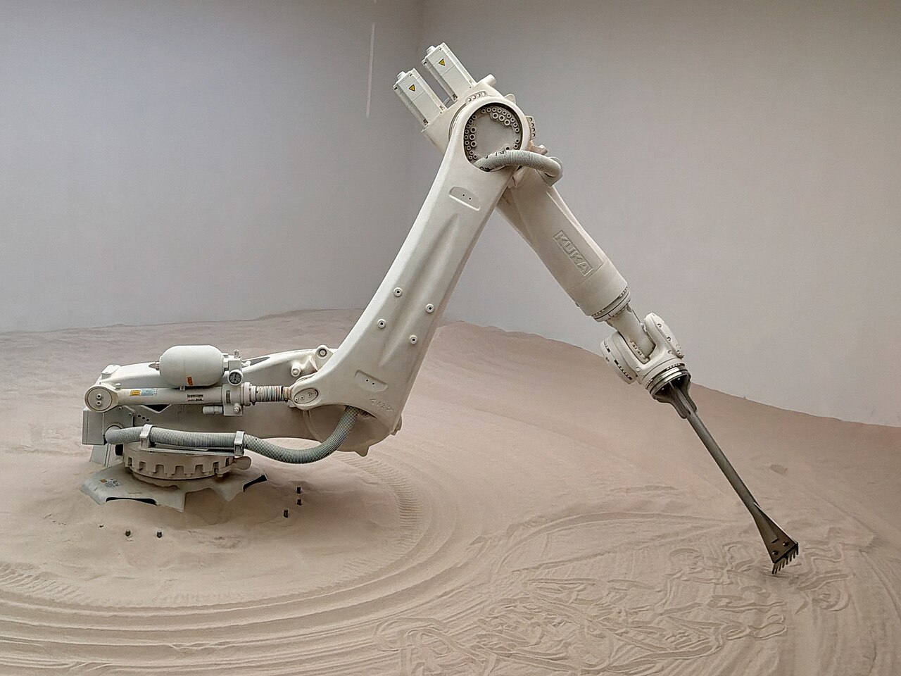 A KUKA industrial robotic arm tracing a pattern in sand