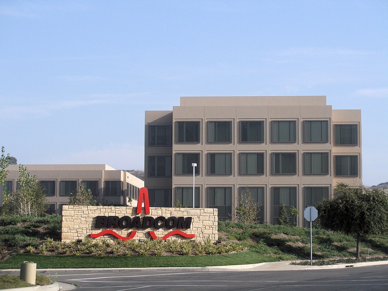 Broadcom headquarters building behind a stone sign with the Broadcom logo