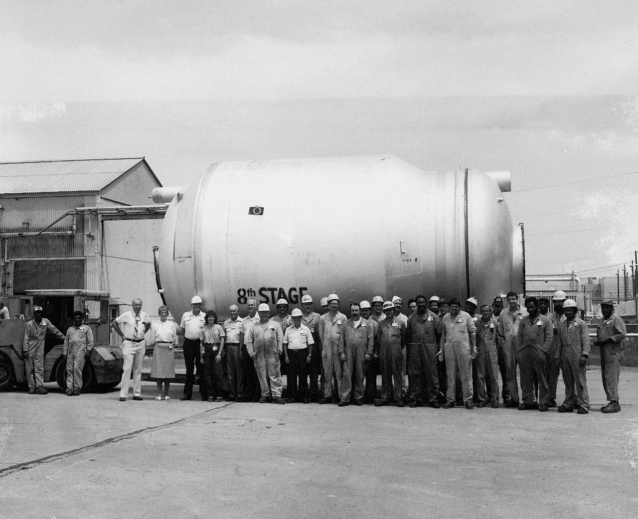 Black and white photograph of plant workers posed beside a large cylindrical uranium-enrichment converter unit labeled 8th Stage at the Paducah Gaseous Diffusion Plant