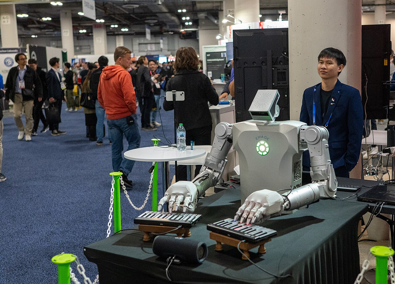 A humanoid robot with articulated hands playing two keyboards at an exhibitor stand on the CES show floor in Las Vegas