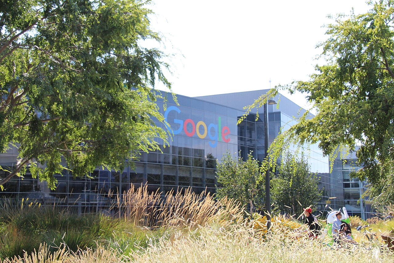 A Google-branded glass office building at the Googleplex in Mountain View, California, framed by trees