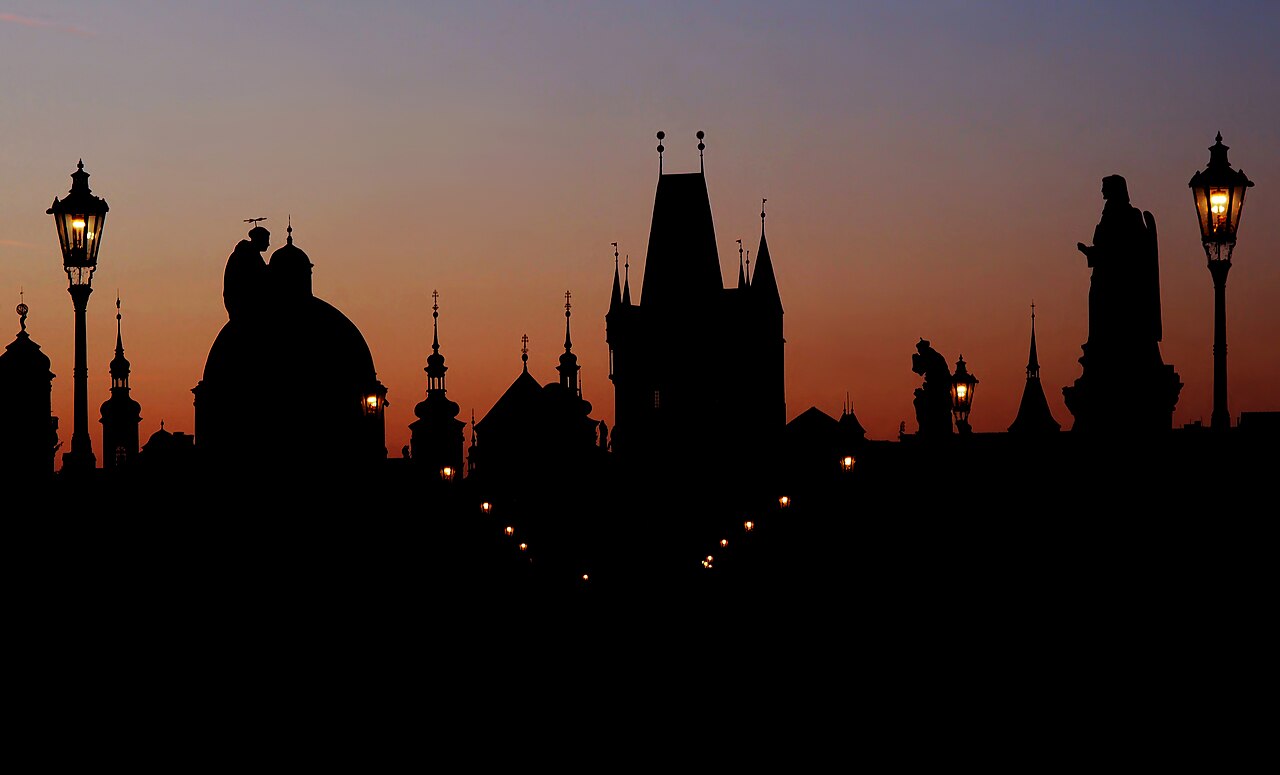 Silhouettes of Prague spires and street lamps at dawn