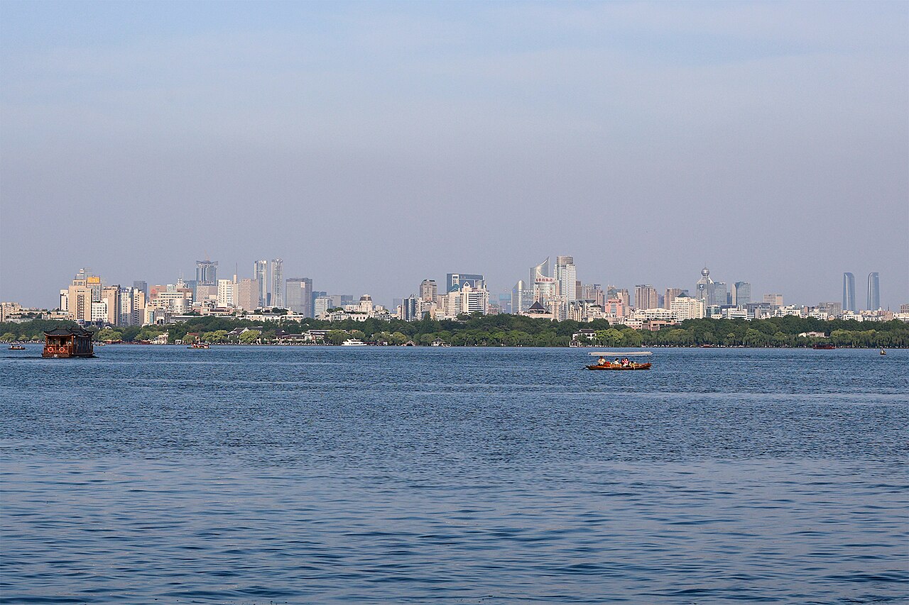 The skyline of Hangzhou, China, seen across West Lake, with modern towers behind a tree-lined shore