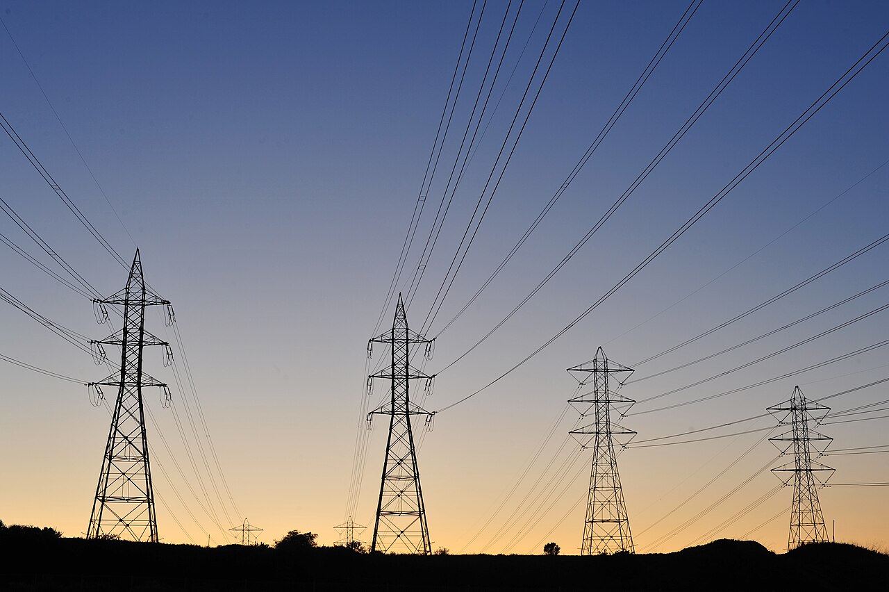 High-voltage electricity transmission towers and power lines silhouetted against a dusk sky