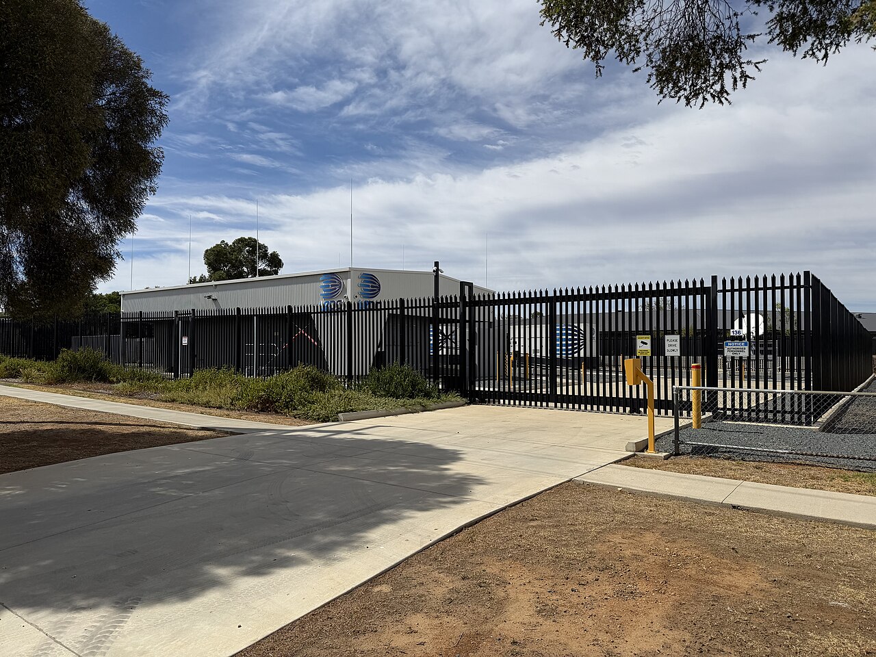 Exterior of an Australian data center facility with security fencing and satellite dishes under a clear sky
