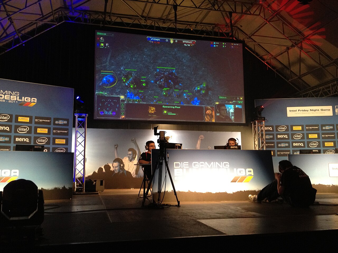 Two StarCraft II players on stage at an ESL event in Munich, with the match shown on a large screen above them
