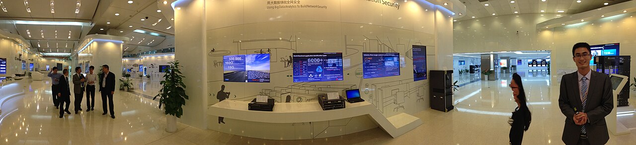 Panoramic view of an exhibition hall at Huawei's site in Shenzhen with display screens and visitors