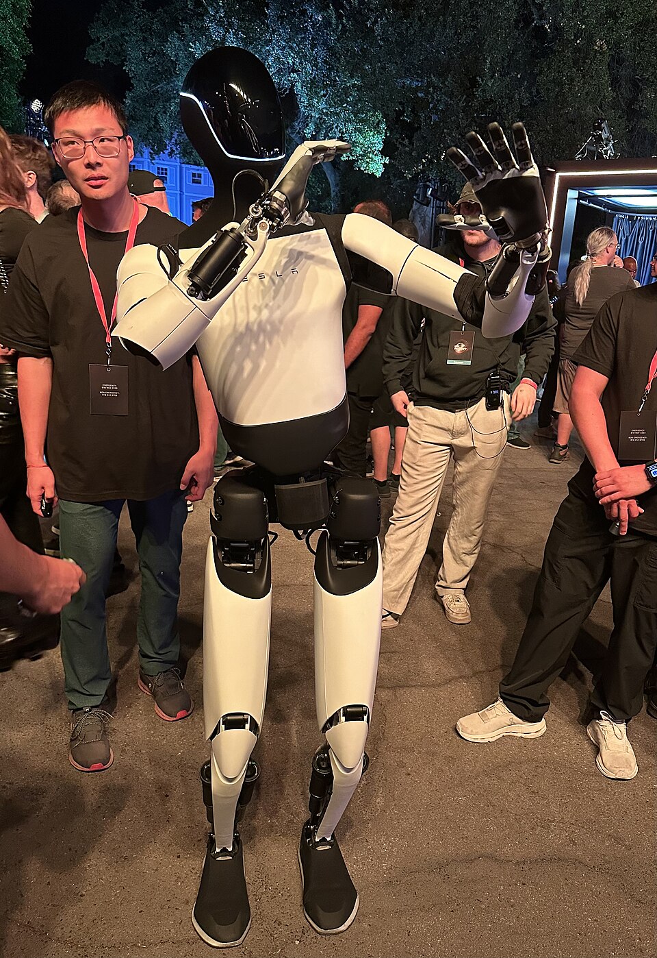 A Tesla Optimus humanoid robot standing among attendees at a Tesla event