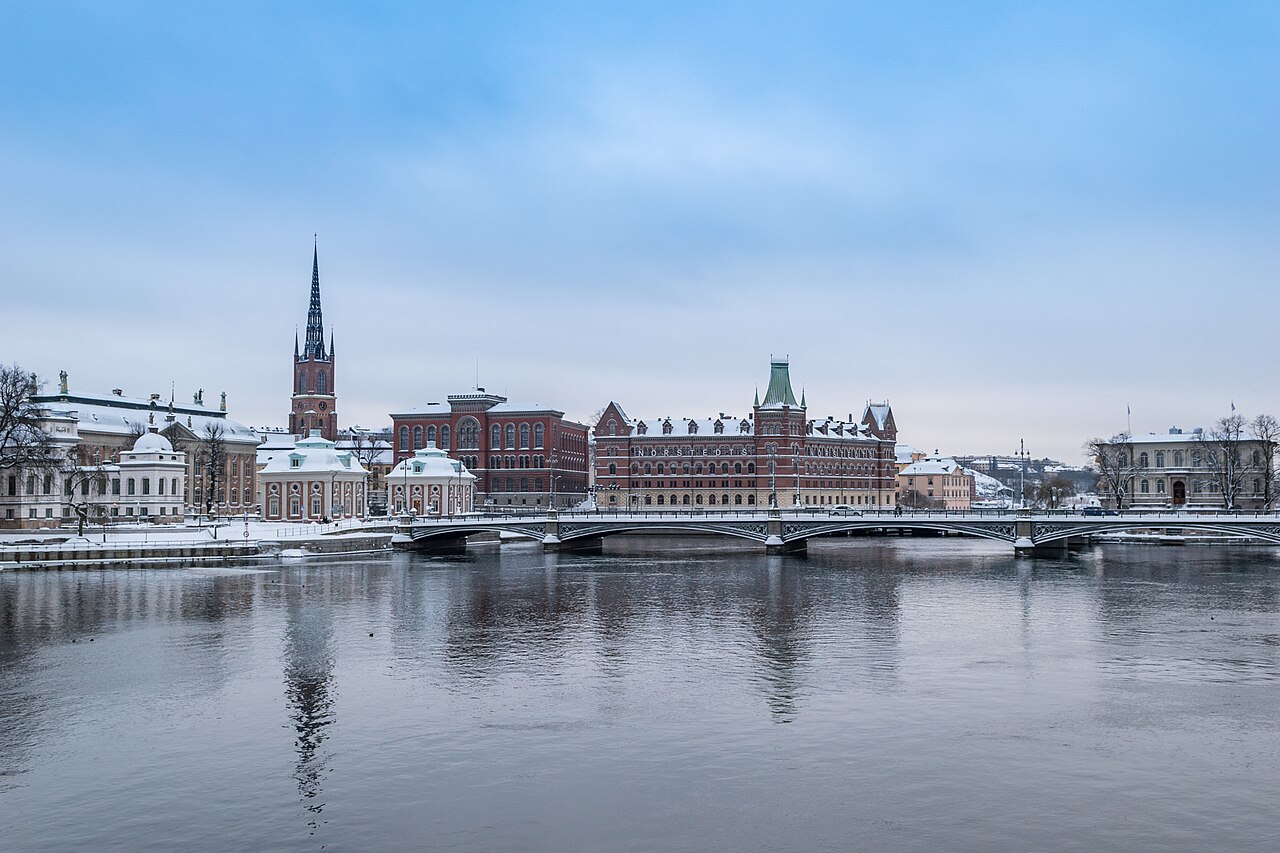 A winter view across the water toward the old town of Stockholm, Sweden, with snow-covered historic buildings and a bridge