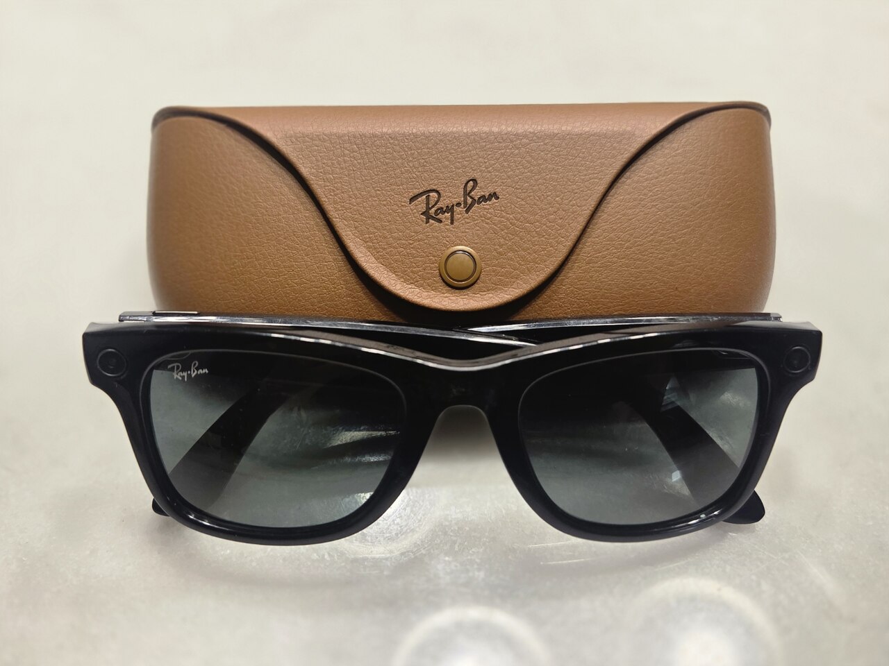 A pair of black Ray-Ban Meta smart glasses in front of a tan Ray-Ban case