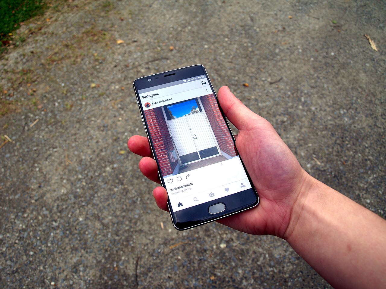 A hand holding a smartphone showing the Instagram app feed