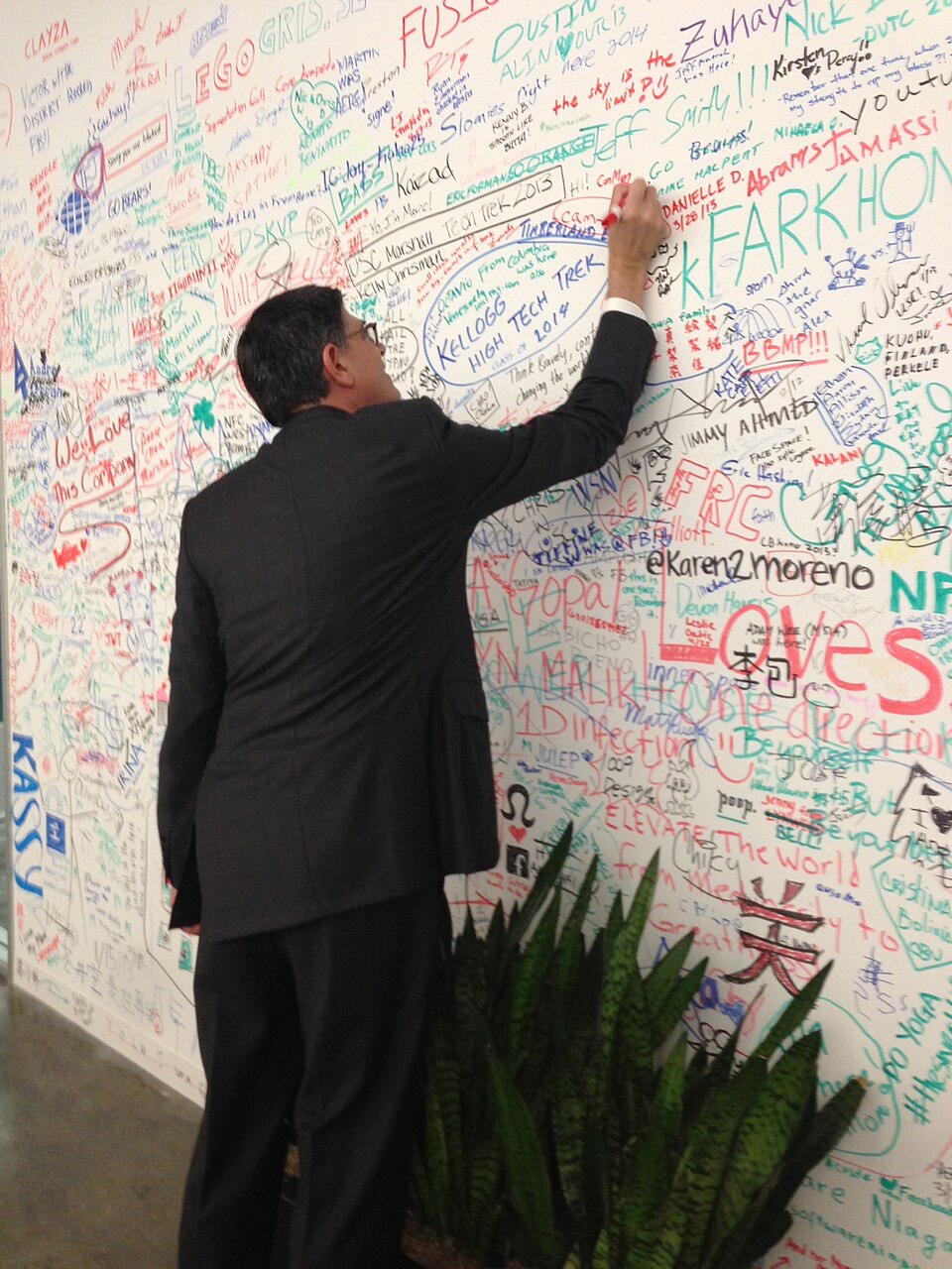 A person in a suit signing a colorful wall covered in handwritten messages at Meta's headquarters