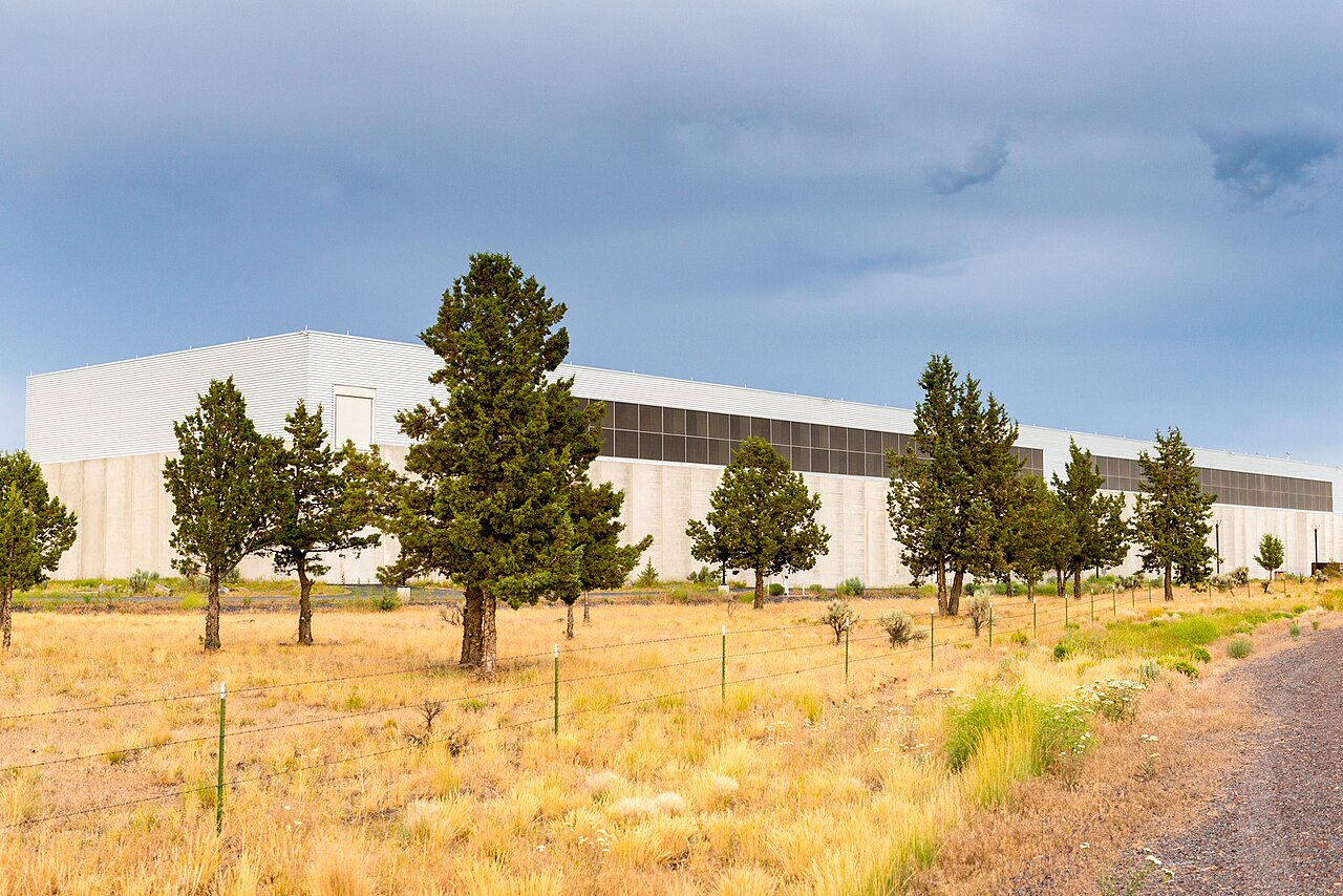 Exterior of a large windowless Facebook data center building behind juniper trees near Prineville, Oregon