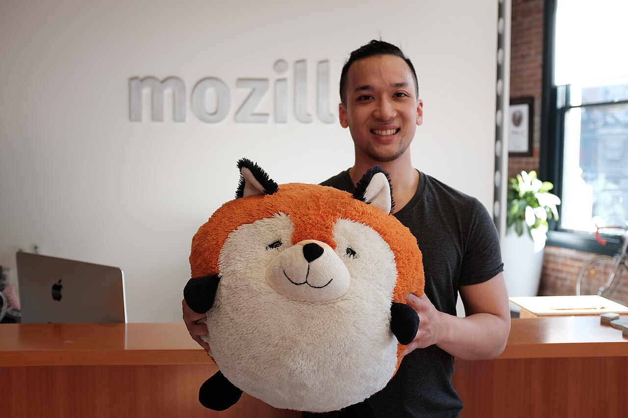 The Firefox fox mascot held up in front of a Mozilla office sign