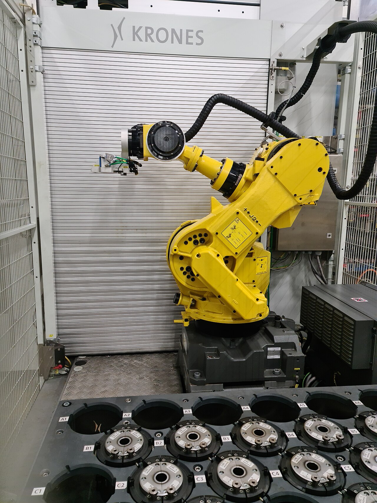 A yellow FANUC six-axis industrial robot arm working inside a caged production cell