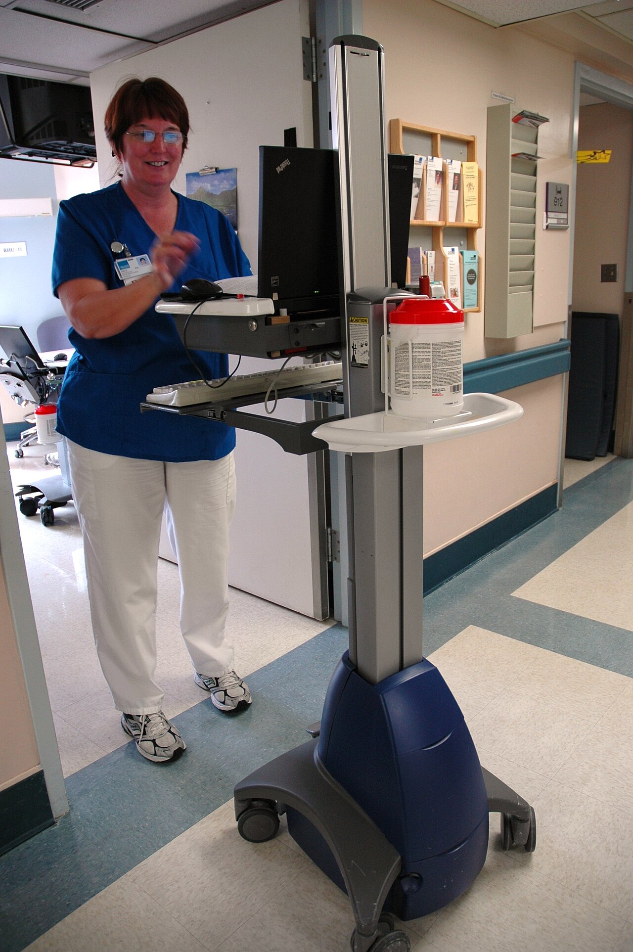 A nurse standing beside a mobile computer workstation in a US hospital hallway