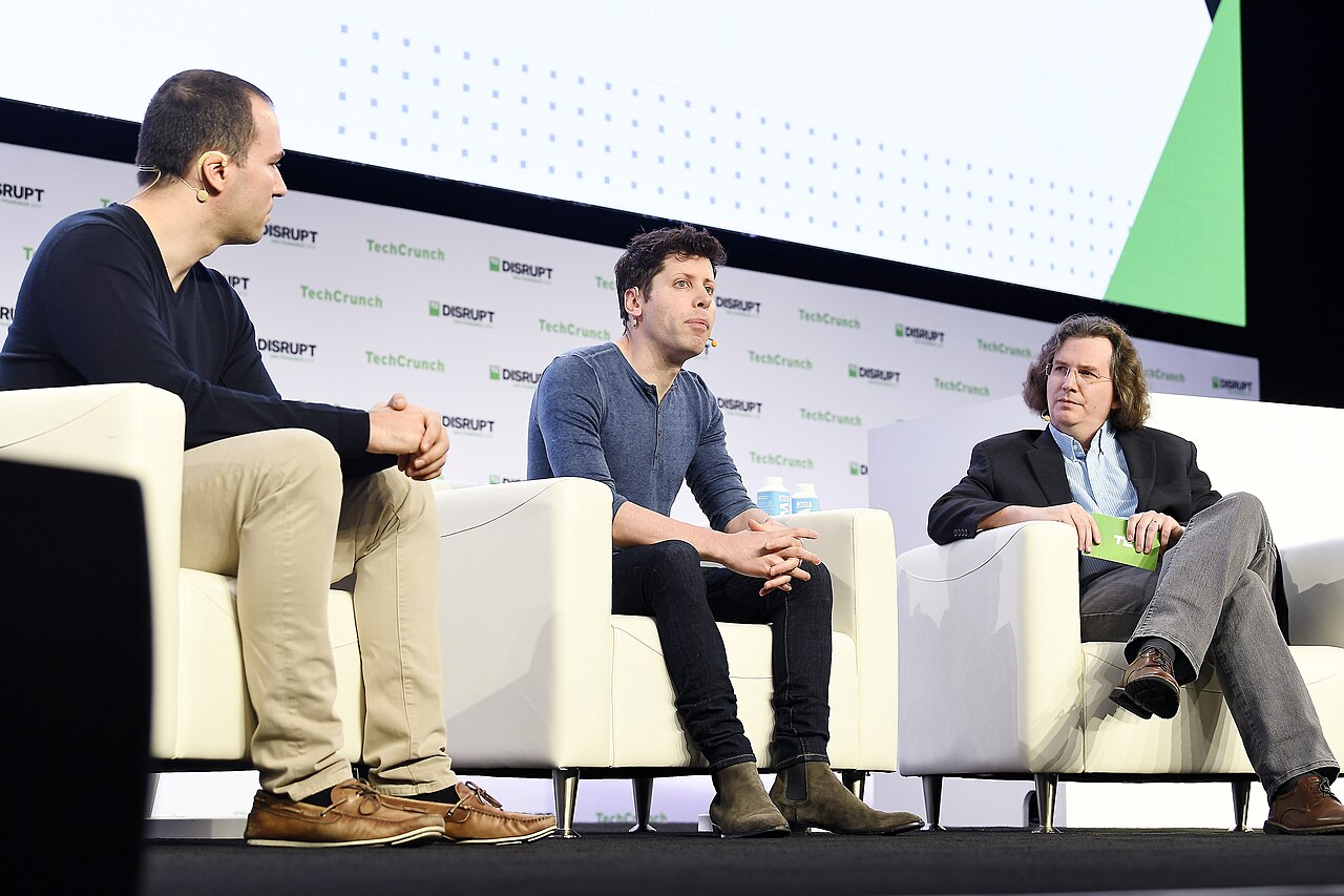Greg Brockman, OpenAI co-founder and Chairman/CTO, seated on stage next to Sam Altman during a TechCrunch Disrupt panel in San Francisco