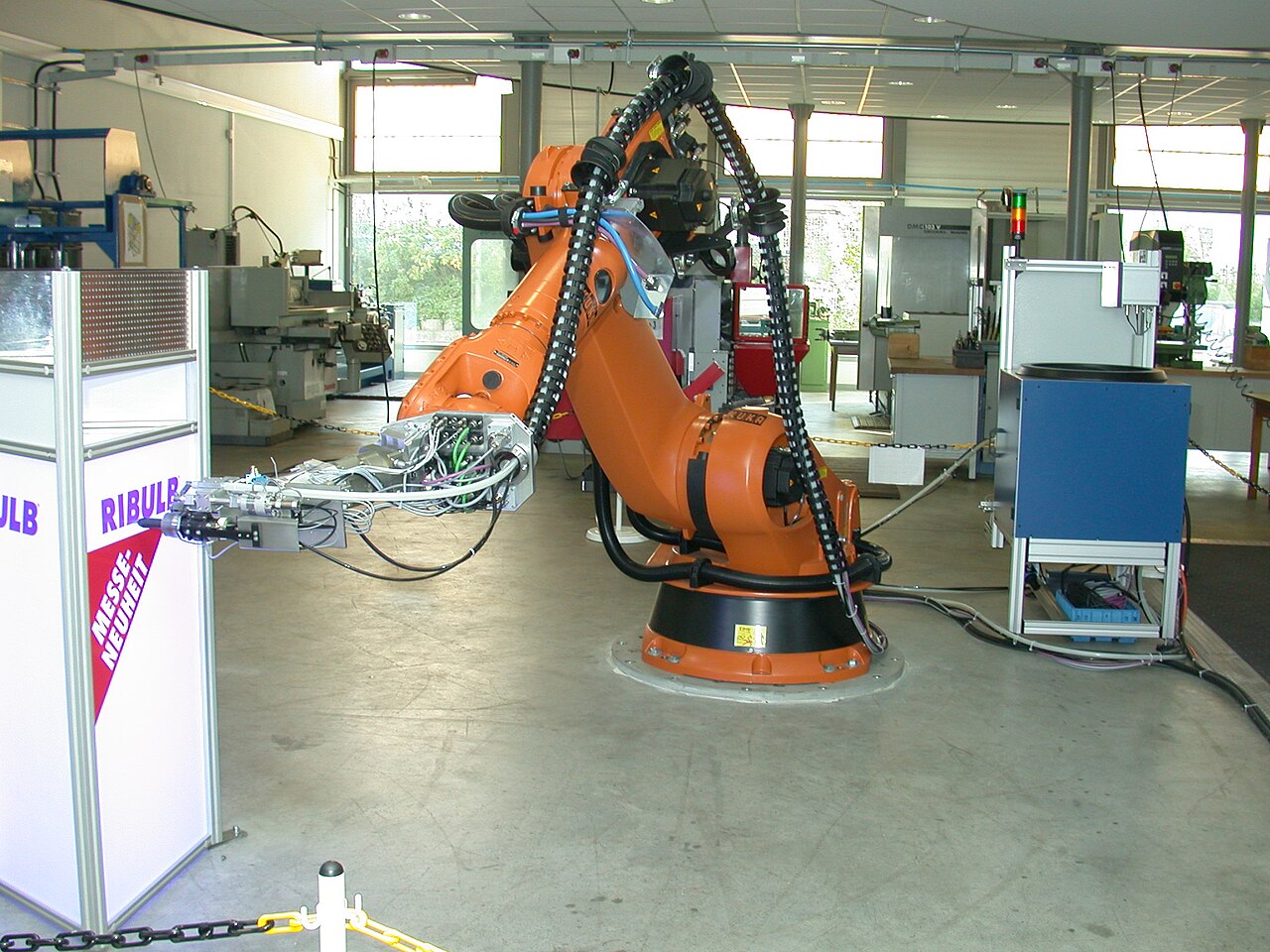 An orange industrial robot arm with a riveting tool mounted on its wrist, standing in a workshop cell