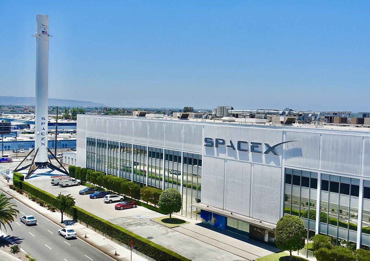 SpaceX's Hawthorne, California factory building with a Falcon 9 first stage standing outside