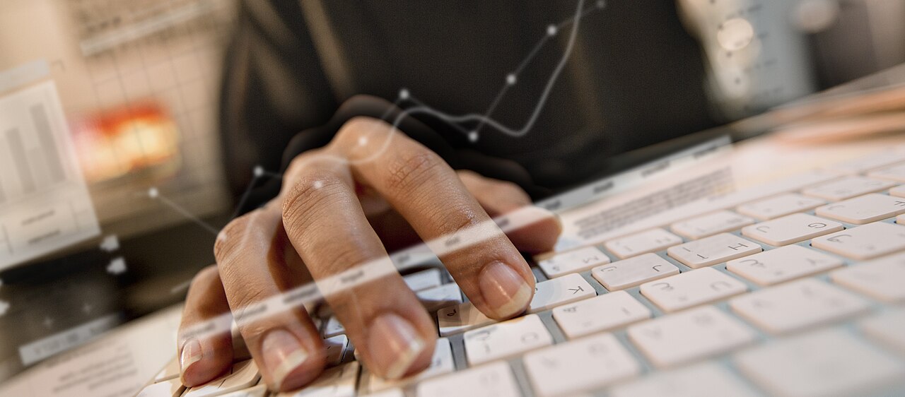 Hands typing on a keyboard with abstract data and chart overlays