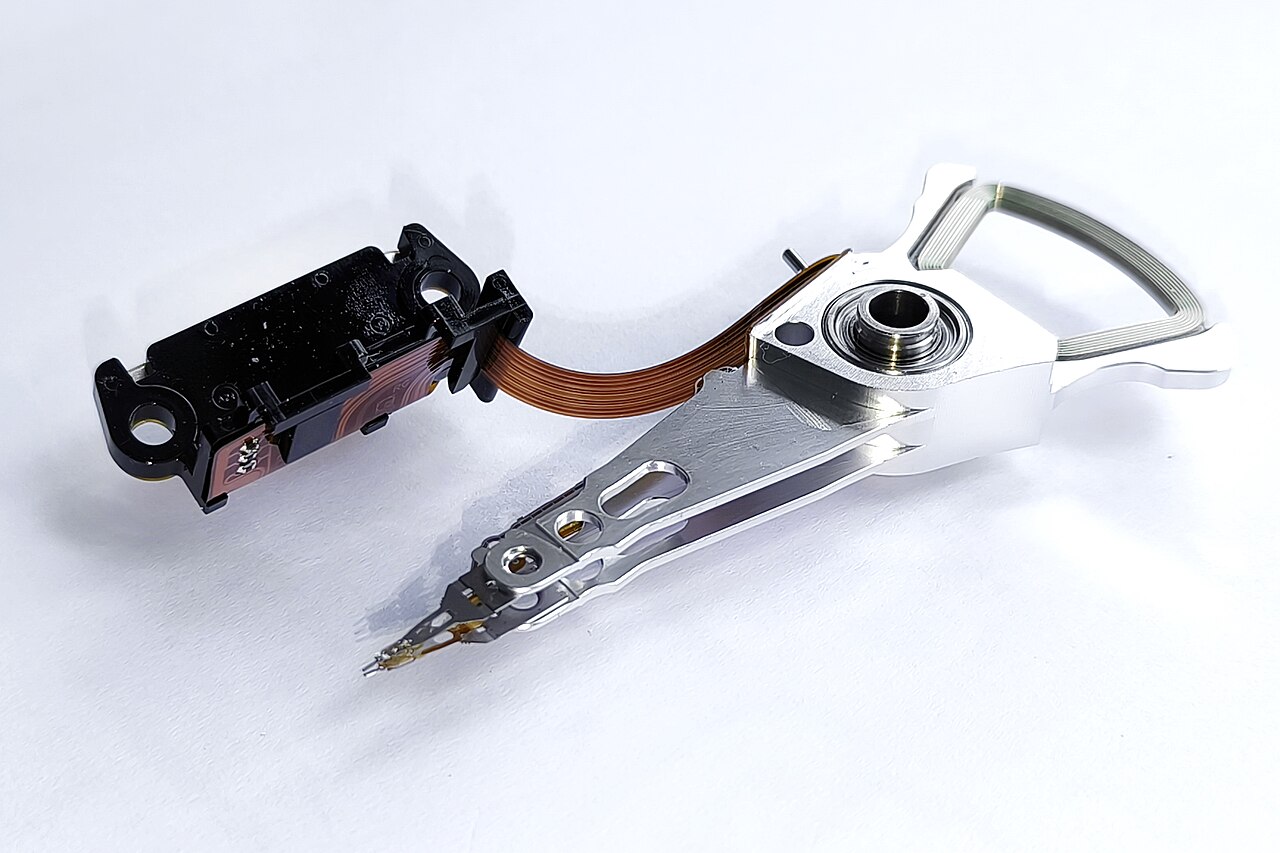 A removed hard disk drive actuator arm assembly with its flex cable and read/write head at the tip