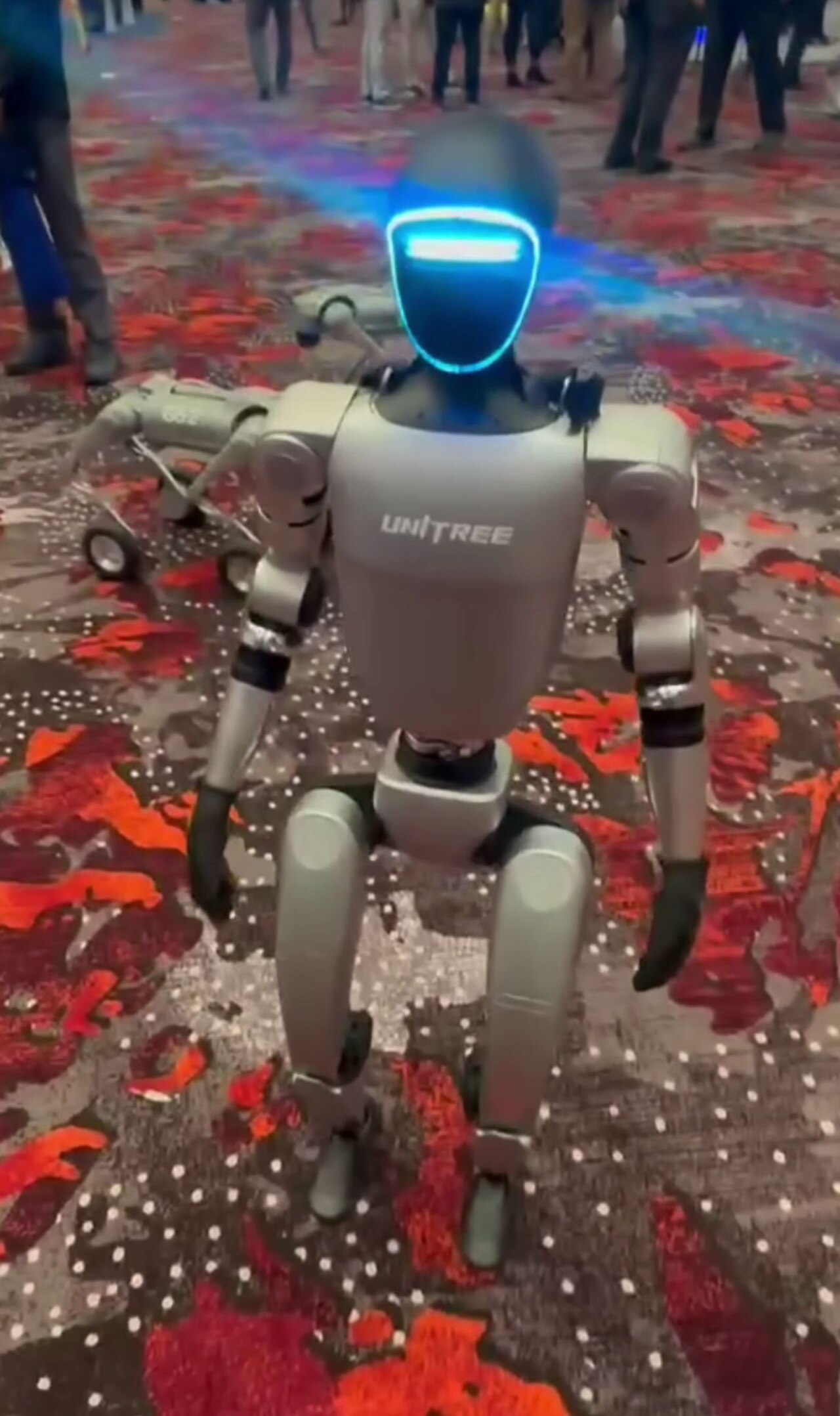 A Unitree humanoid robot with a glowing visor standing at an event