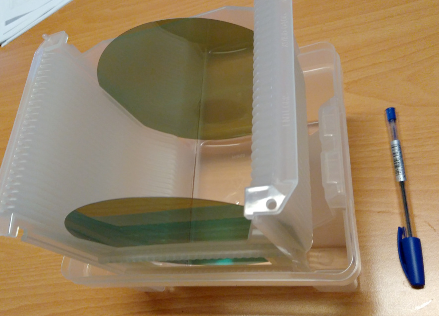 Silicon carbide wafers in a clear plastic carrier on a wooden desk, with a pen beside it for scale